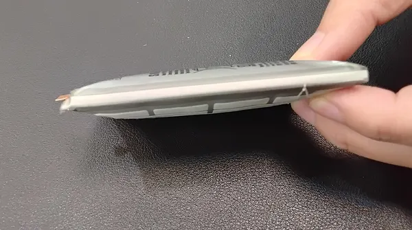 Batería de celular hinchada vista de costado, curvada en el centro